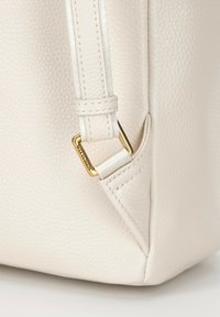 Bílá texturovaná kožená kabelka s jemným zrnitým vzorem, vybavená zlatými kovovými akcenty na bílém řemínku.