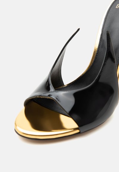Λαμπερό μαύρο σανδάλι με ανοιχτά δάχτυλα και ψηλό τακούνι, με χρυσή εσωτερική σόλα και κομψές, κυρτές λεπτομέρειες στο πάνω μέρος.