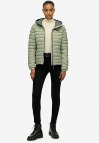 Lysgrøn pufferjakke med hætte, lynlås foran og quiltet design, parret med sorte skinny jeans og sorte snørebåndsstøvler.