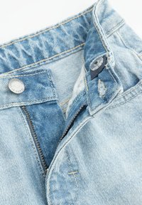 Jasnoniebieskie dżinsy, z zapięciem na guzik i zamkiem błyskawicznym. Krawędzie są przeszyte kontrastową nitką; delikatne przetarcia na tkaninie.