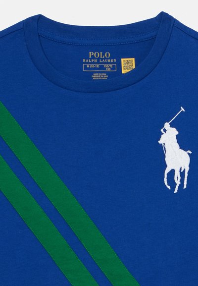 Mėlynos medvilnės marškinėliai su dviem žaliais įstrižais raštais, balta išsiuvinėta polo žaidėjo logotipu ir klasikinėmis apvalios kaklo iškirptėmis.
