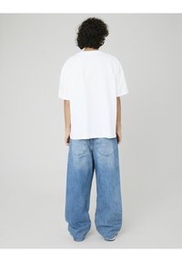 T-shirt blanc à manches courtes associé à un jean baggy bleu clair, doté d'un délavage et de poches arrière. Design simple et décontracté.