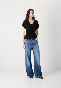 Black short-sleeved top with ruched texture and v-neck, paired with oversized blue denim jeans and black pointed-toe shoes.