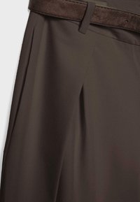 Close-up of dark brown tailored trousers with a matching suede belt threaded through belt loops.