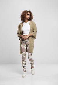 Maslinasto zeleni kimono jakna, bijeli skraćeni top, legins s kamuflažnim uzorkom u bež i zelenim tonovima, te bijele tenisice s niskim profilom.