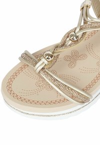 Sandalo dorato con cinturini glitterati e perline decorative. Sottopiede morbido beige con motivi floreali. Suola bianca testurizzata con accenti argentati.
