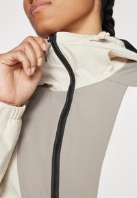 Chaqueta ligera y multicolor con un alto cuello, cremallera frontal y puños elásticos; presenta una textura suave y acentos negros contrastantes.