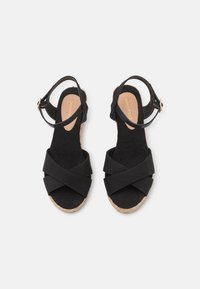 Sandales en tissu noir avec des brides croisées, une bride de cheville ajustable et une semelle en liège. Semelle intérieure texturée avec un détail de logo.