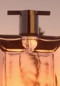 Klart glass parfymeflaske med rektangulær form. Metallisk sølvpumpe og hette. Væsken har en myk ravfarge som reflekterer lyset.