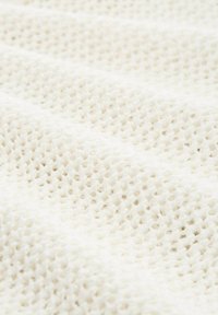 Weißer Strickstoff mit einem strukturierten, offenen Webmuster, das ein weiches Aussehen und eine leicht erhabene Oberfläche zeigt.