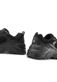 Schwarze Sportschuhe mit einer strukturierten Oberseite und einer dicken Gummisohle, in runder Form und mit sichtbar akzentuiertem Logo an der Ferse.