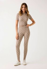 Bēša rakstaina sporta apģērbu komplekts ar īsām piedurknēm un augsta vidukļa legingi, ar baltu apmali un teksturētu audumu.