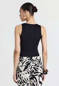 Body nero senza maniche abbinato a pantaloni a vita alta con stampa zebrà in bianco e nero. Design semplice e texture liscia.