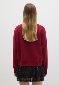 Rode cropped sweatshirt met lange mouwen, gecombineerd met een zwarte met sequins bedekte gelaagde rok, die een textuur en glanzende afwerking laat zien.