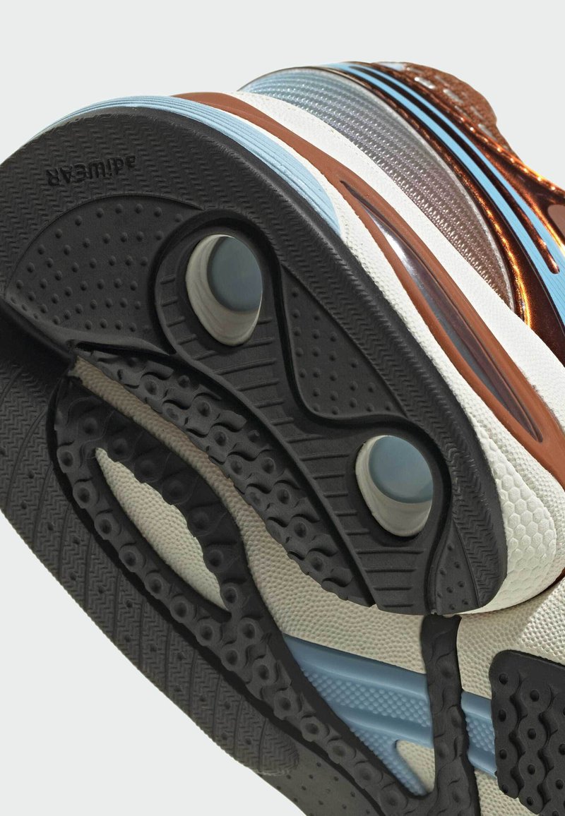 Baskets avec une semelle en caoutchouc noire, une semelle intermédiaire blanche texturée, des accents marron et des rayures bleues; comprend des éléments de coussin d'air visibles.