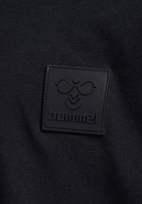 Czarny sportowy top wykonany z gładkiego materiału, z czarną gumową naszywką z wytłoczonym logo.