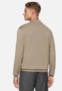 Maglione beige a maglia con maniche lunghe e polsini a coste, dotato di un colletto alto e tessuto texturizzato, abbinato a pantaloni grigio scuro.