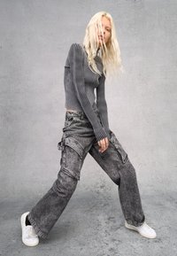 Grijze geribde longsleeve top gecombineerd met hoogzitter, wijde cargo jeans met een versleten denimlook en zijzakken, afgewerkt met witte sneakers.