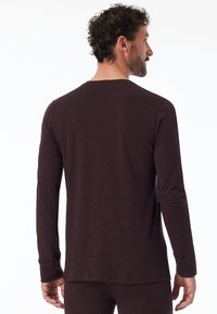 Langärmliges, dunkelbraunes Oberteil aus weichem Material. Verfügt über einen runden Halsausschnitt und eine figurbetonte Silhouette, mit einem leicht geschwungenen Saum hinten.