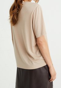 Béžový top s krátkým rukávem a jemným leskem, volný střih a kulatý výstřih. V kombinaci s tmavou koženou sukní, která se vyznačuje hladkou texturou.