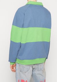 Pull en coton avec des rayures horizontales bleues et vertes, un col, et des poignets côtelés. Coupe décontractée avec une surface texturée.