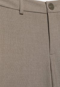 Zbliżenie na pas beżowych spodni materiałowych z zapięciem na guzik, szlufką na pasek i detalem kieszeni.