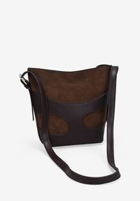 Bolso cruzado de ante y cuero marrón con un diseño curvo, correa larga y acentos de cortes circulares en la parte delantera. Textura suave.