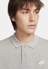 Világosszürke pólóing gallérral, két gombbal és egy kis fehér Nike logóval a bal mellen. Texturált anyag, normál szabás.