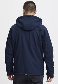 Veste bleu marine avec capuche ajustée, fabriquée en matériau doux et texturé. Équipée de poignets élastiques et d'un ajustement à la taille par cordon.