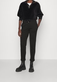 Černý fleecový pulovr se zipovým límcem a kroužkovým zapínáním, spárovaný s černými tepláky s regulovatelným pasem a bočními kapsami, oblečený s robustními černými botami.