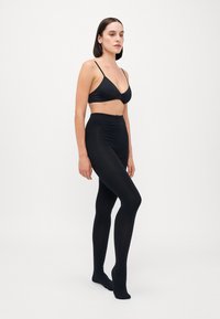 Sort sømløs bh med tynde stropper, parret med højtaljede sorte tights. Begge er lavet af glat, strækbart stof og tilbyder en tætsiddende pasform.