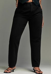 Hoge zwarte denim jeans met rechte pijpen, vijf-vakken ontwerp en subtiele stikseldetails, gecombineerd met zwarte haksandalen.