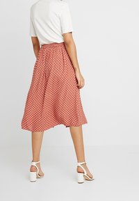 Falda midi de lunares rojos con cintura elástica, hecha de tela ligera, combinada con sandalias de tacón cuadrado blancas.