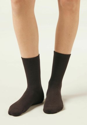 Legs wearing mid-calf, ribbed black socks standing on a light-colored floor with a plain background.