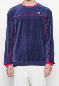 Námořnický modrý sametový svetr s červenými pruhy na ramenou a rukávech, s kulatým výstřihem a logem na hrudi.