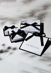 Three gift boxes in white with black accents and ribbons, featuring the logo "LATELITA." Varying sizes arranged with shadows on a surface.