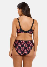 Femme vue de dos portant un soutien-gorge floral noir et une culotte taille haute assortie, avec de longs cheveux bruns lâchés.
