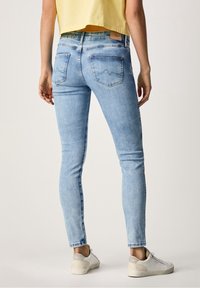 Vaqueros ajustados de color azul claro con una textura de denim suave, cintura de media altura, dos bolsillos traseros y sutiles detalles de costura. Combinados con zapatillas blancas.