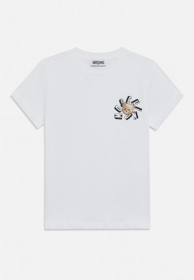 T-shirt bianca a maniche corte con piccola faccia di orsetto e lettere nere che formano la parola "Moschino" intorno alla stampa sul lato sinistro del petto.