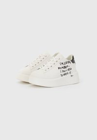 White canvas sneakers with a chunky sole, featuring black handwritten text on the side and a black accent on the heel.