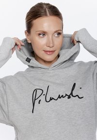 Szara bluza z kapturem, z czarnym haftowanym napisem. Miękki materiał o luźnym kroju i ściągaczach na rękawach. Metka widoczna na wewnętrznej stronie kołnierza.