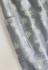 Tela gris con una superficie texturizada, con un patrón floral blanco. Incluye un bolsillo con un delicado detalle de costura.