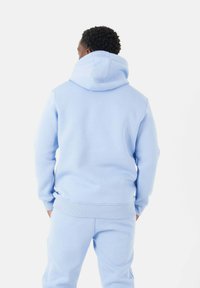 Felpa con cappuccio blu chiaro realizzata in tessuto morbido, dotata di tasca a marsupio e polsini a costine. Il design è minimale, senza loghi visibili.