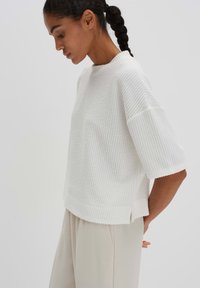 Witte gebreide top met korte, wijde mouwen en een ribbelstructuur. Heeft een ontspannen pasvorm en een ronde halslijn. Gestyled met lichte broek.