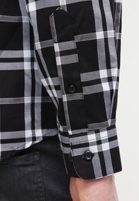 Svartvit rutigt skjortsärm med knappdetalj, som visar distinkta rutig mönster och en vikt manschett.
