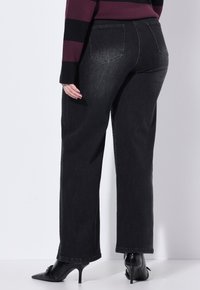 Pantaloni in denim nero a gamba dritta con tasche posteriori, abbinati a tacchi neri. Presentano una texture liscia e un design classico.