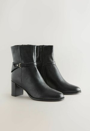 Bottes noires à talons, arrivant mi-mollet, avec texture peau de serpent, fermeture éclair sur le côté et sangle décorative avec petite boucle métallique.