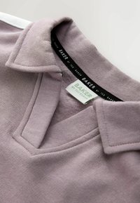 Lilla polo t-shirt med krave, der har et tekstureret stof og en mærkat med teksten "BAKER by Ted Baker." Pæn syning og blødt materiale.