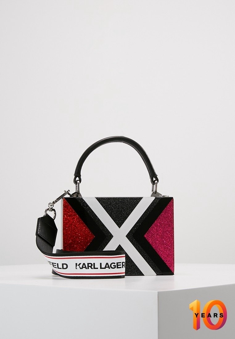 Borsa multicolore scintillante con manico nero, caratterizzata da motivi geometrici rosa, rossi e bianchi, e tracolla rimovibile con logo.