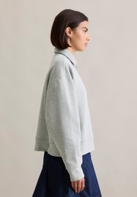 Light gray, oversized sweatshirt with a collar and ribbed cuffs. Features dropped shoulders and a relaxed fit. Smooth cotton texture.